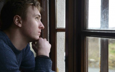 Un joven que sufre de depresión mira por una ventana pensando en el día que tiene por delante. Fotografía: Newscast Online. 