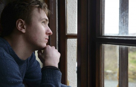 Un joven que sufre de depresión mira por una ventana pensando en el día que tiene por delante. Fotografía: Newscast Online. 